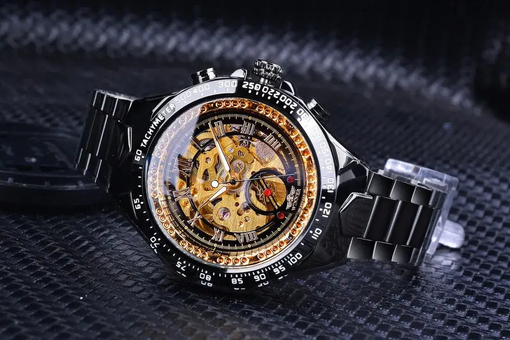 Black stainless steel Winner mechanical sport chronograph watch with gold skeleton dial, Roman numerals, and gemstones.